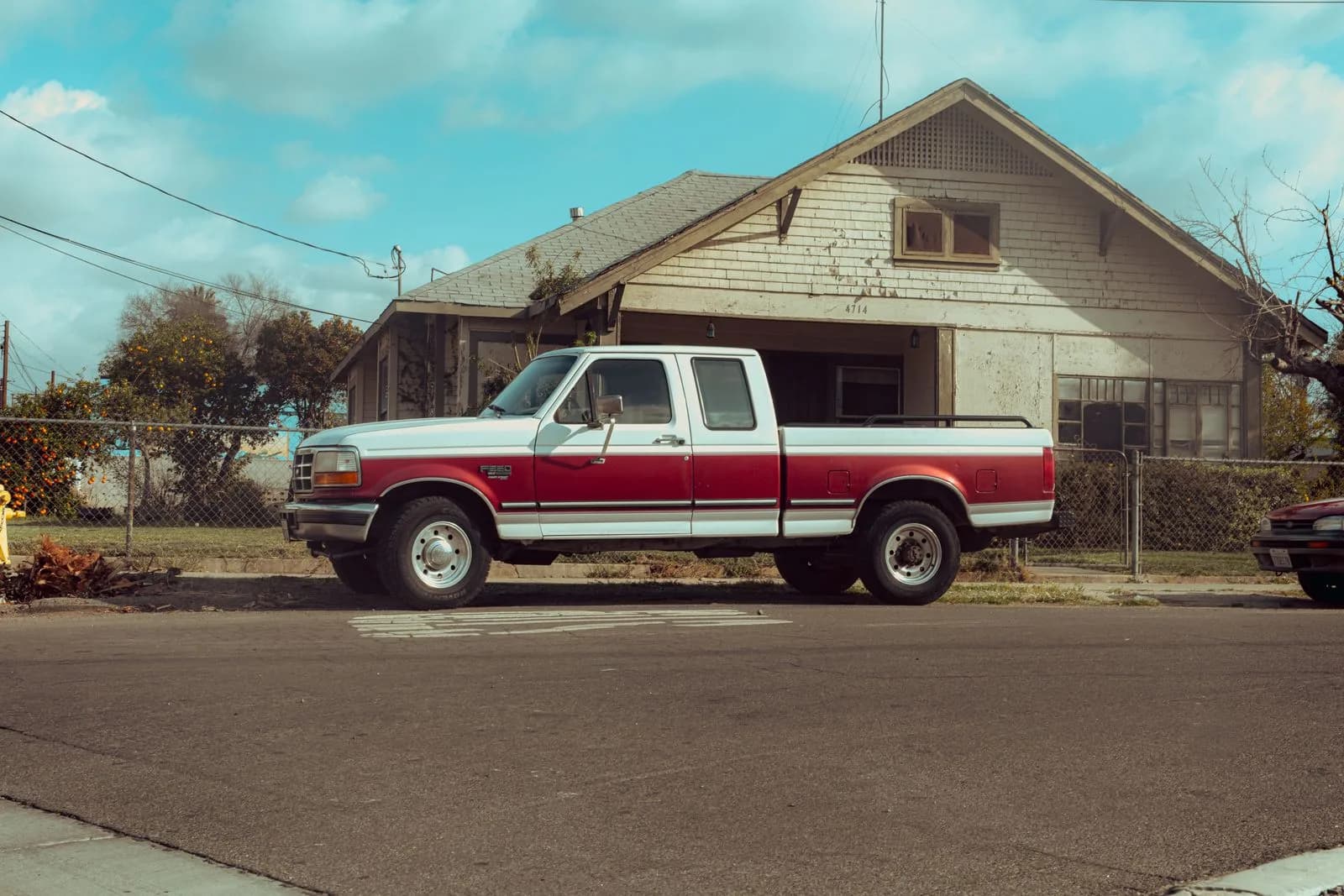 Red and white full-size pickup truck with a long bed parked outside a house